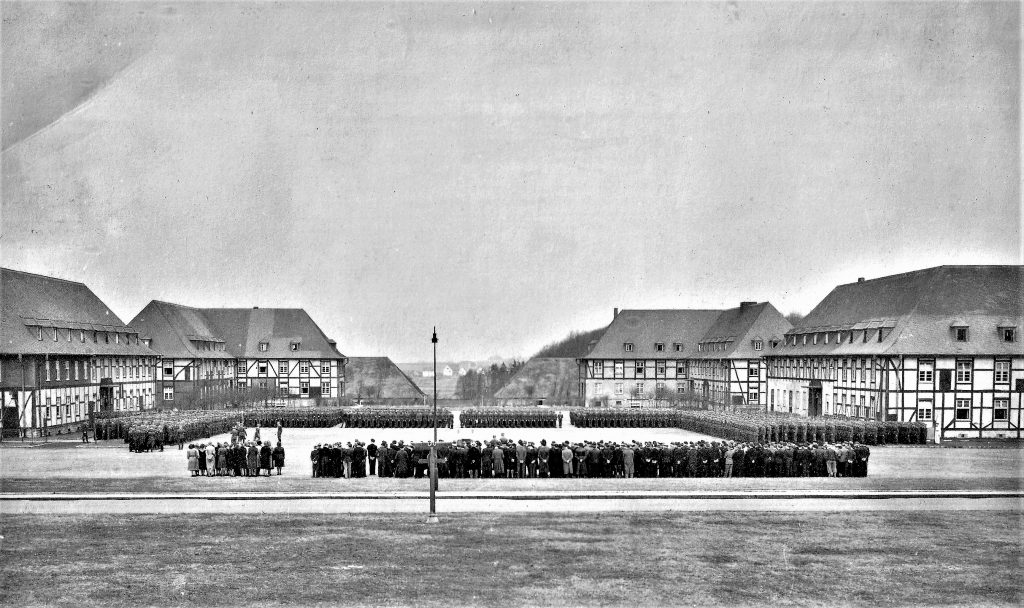 Exerzierplatz des Flugplatzes Detmold bei einer Zeremonie um 1943. Die Kasernengebäude sind aus Gründen der Tarnung mit einer Fachwerk-Illusion versehen.